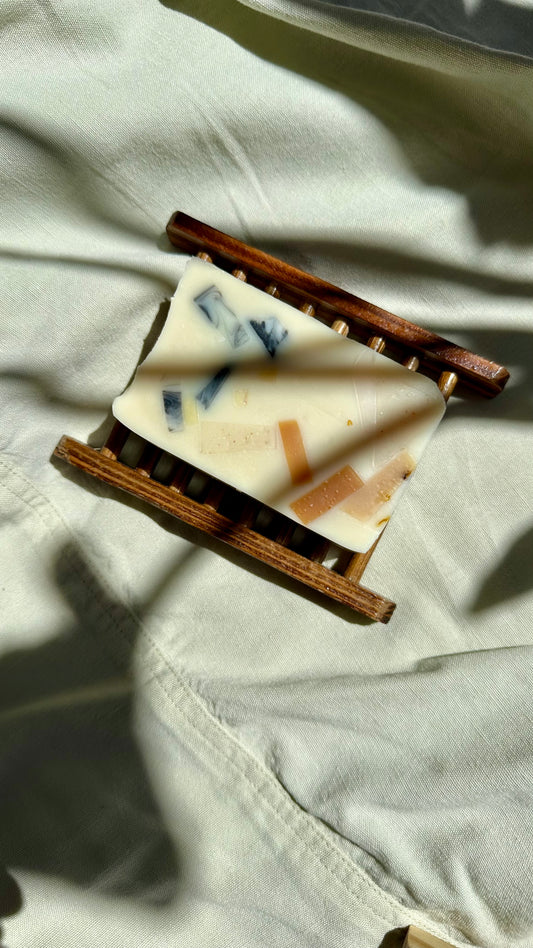 A rectangular soap bars with blue and white patterns on a wooden soap dish, placed on a light-colored fabric background.