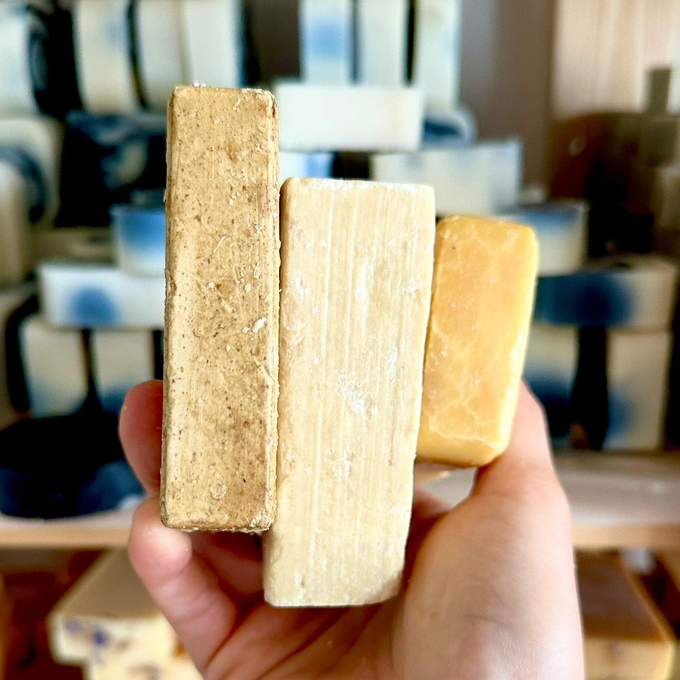 Hand holding three wooden blocks with a blurred background of stacked boxes.