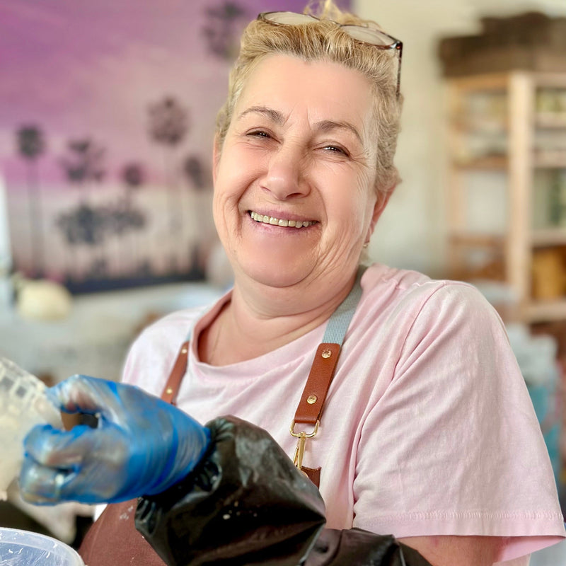 Woman in a pink shirt and apron holding a black bag, with a blurred background